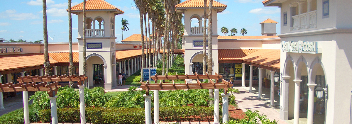 Outdoor shopping center with palm trees and arches.