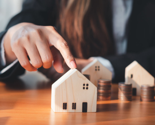 Hand touching wooden house model with coins.