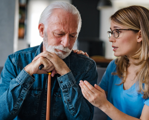 Woman comforting elderly man with cane.